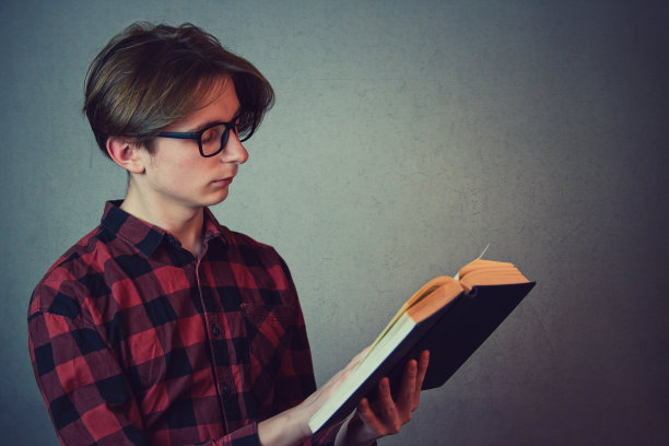 戴眼镜的男学生在灰色背景前读书图片下载