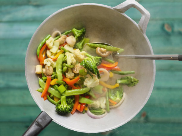 在绿松石色的木桌背景下，在热气腾腾的炒锅里翻炒各种新鲜的蔬菜。图片下载