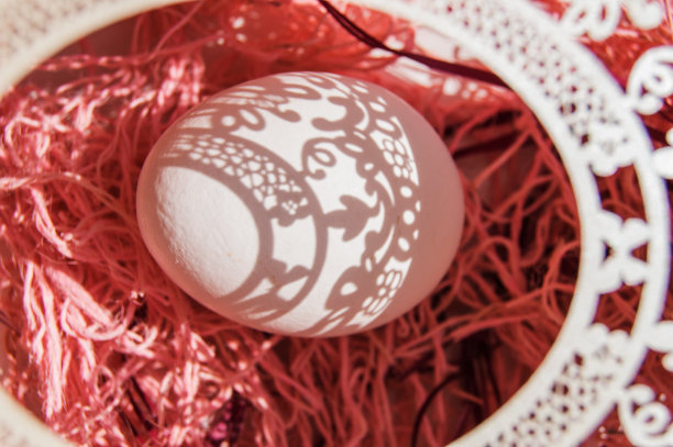 俯视：粉色背景上纸质镂空框架中的白色复活节彩蛋，阳光明媚图片下载