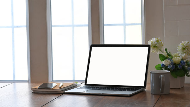 白色空白屏幕笔记本电脑、咖啡杯、笔记本、钢笔和盆栽放在现代木桌上的照片，透过窗户的光线作为背景。图片下载