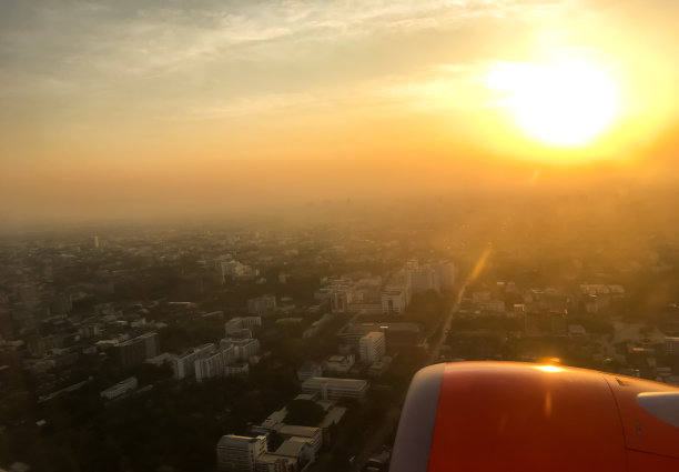 从窗口看，看到机翼的飞机飞行与城市和天空的背景。从飞机窗口观看早晨的天空。俯视图城市背景。图片下载