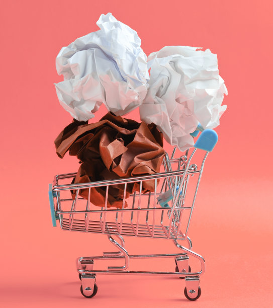 办公室业务概念。粉红色背景的迷你购物车里的皱巴巴的纸球。图片下载