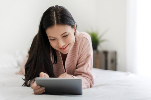 女人在家里的床上放松，使用平板电脑。女人查看社交应用和工作。沟通和科技概念图片下载