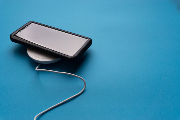 在蓝色背景的充电板或基座上充电的智能手机。图片下载