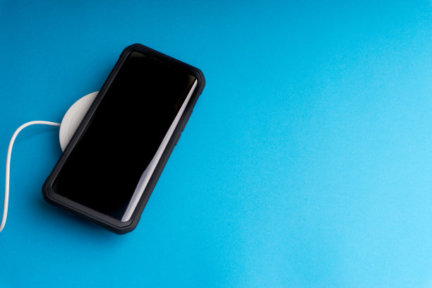 在蓝色背景的充电板或基座上充电的智能手机。图片下载