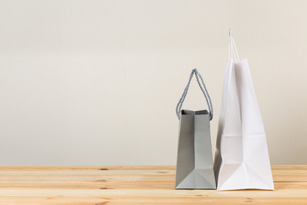 一个带把手的购物空纸袋，在一个浅木桌子的正面右侧，有一个浅墙背景图片下载
