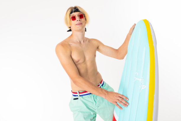 一个英俊的金发男人，白色背景上的冲浪板形状的充气游泳床垫图片下载