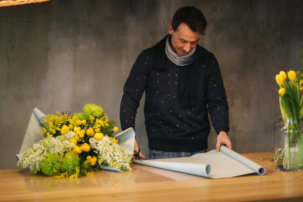 男作春花束。一个花商在木桌上用包装纸包装着一束美丽的春天鲜花。美丽的花组成黄花图片下载