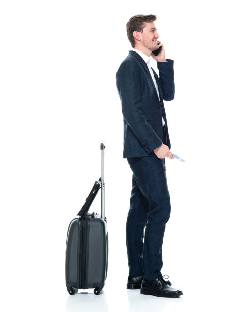 白人年轻男性商人站在白色背景前，穿着智能休闲装，拿着行李，使用智能手机图片下载