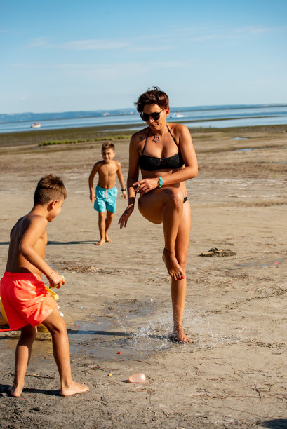 顽皮的男孩扔水炸弹在年轻的女人在沙滩上-库存照片图片下载