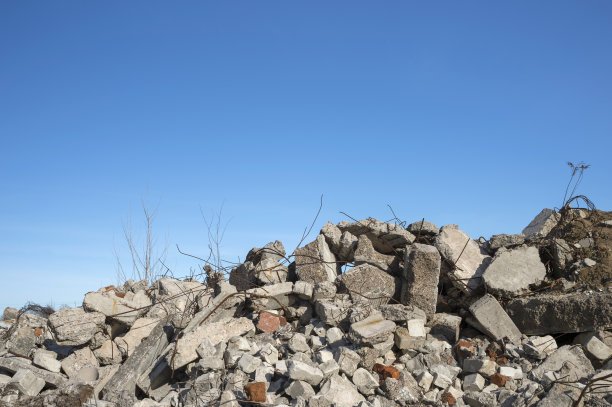 一堆巨大的灰色混凝土碎片和突出的配件映衬着蓝色多云的天空。背景。图片下载
