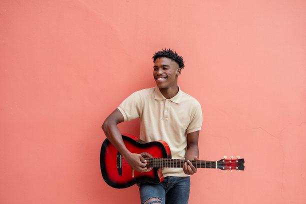 站在彩色墙壁前抱着吉他的年轻男人图片下载