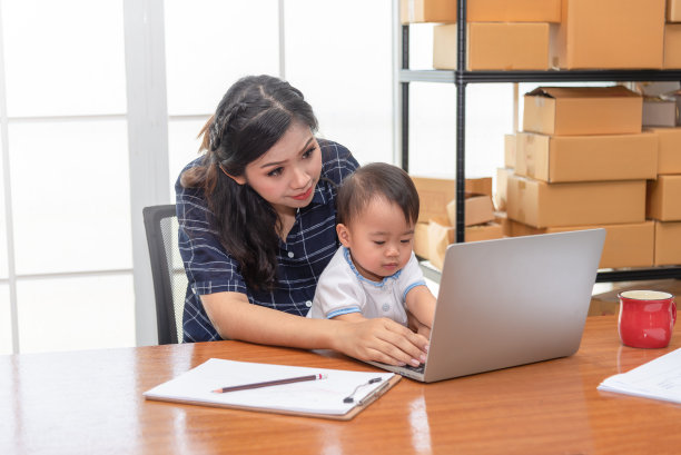 年轻漂亮的单身妈妈在家里用笔记本电脑工作，而小女儿需要她的关注。妈妈和女儿玩笔记本电脑。图片下载