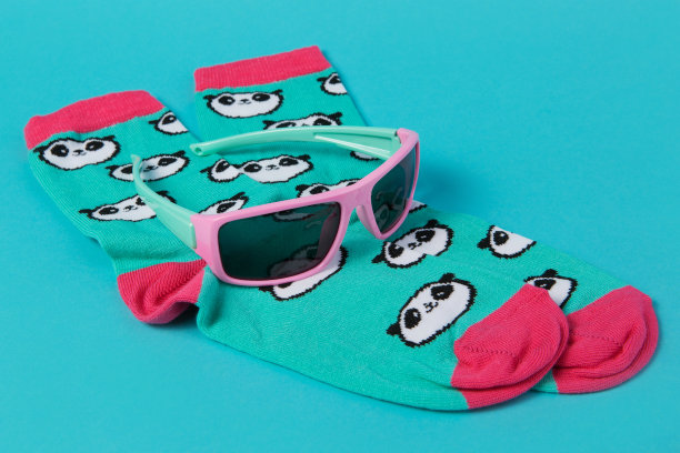 一双有着熊猫脸图案的绿松石袜子，躺在绿松石背景上，墨镜在上面，这就是度假的概念图片下载