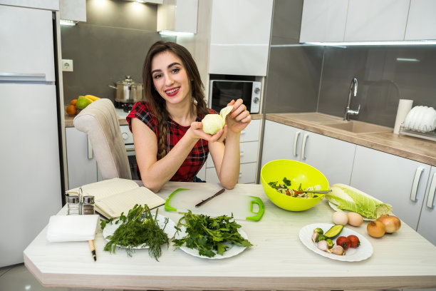 为了健康的生活方式，女孩在餐桌前摆姿势，同时准备用不同的蔬菜和绿色蔬菜做成的沙拉。图片下载