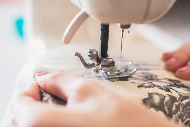 在家缝制窗帘的过程：缝纫机上的窗帘带特写，卷边、剪裁、修理和缝合布料和连衣裙，背景是女裁缝的手图片下载