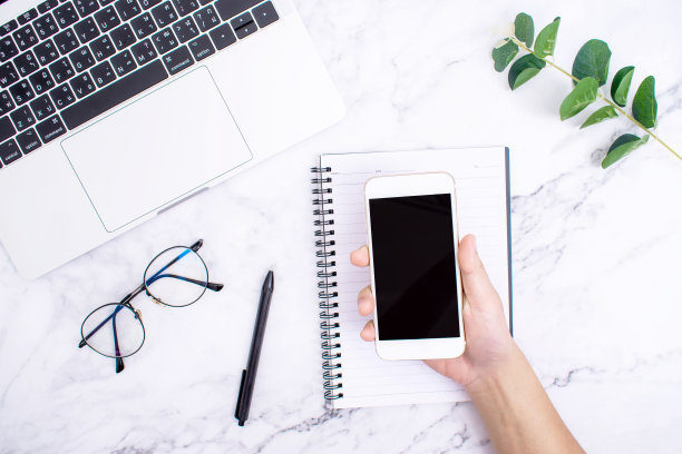 现代办公桌俯视图：眼镜、笔、笔记本电脑，以及带有黑色屏幕智能手机的模型图片下载