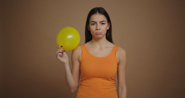 心烦意乱的年轻女子吹气球孤立的棕色背景图片下载