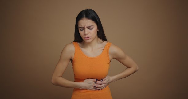 一位棕色背景下的年轻漂亮女子感到胃痛图片下载