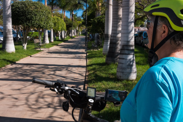 运动妇女70岁的休息在一个公共公园与她的电动自行车。健康的生活方式。背景是热带植物。图片下载