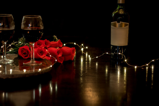 红酒和玫瑰放在暗色的餐桌上，为浪漫的晚餐约会夜献上心焦图片下载