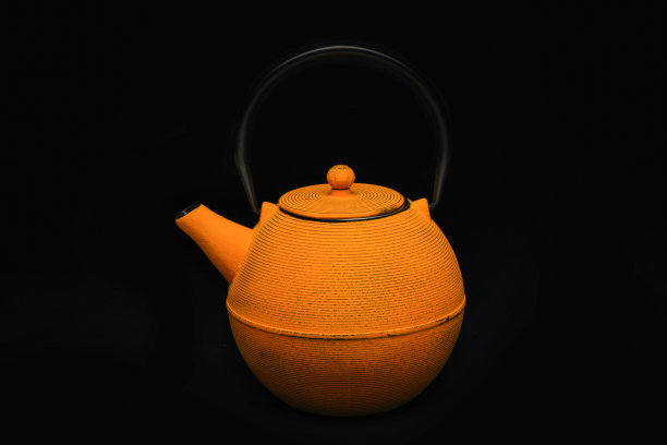 黑色背景上的黄色铸铁茶壶。图片下载
