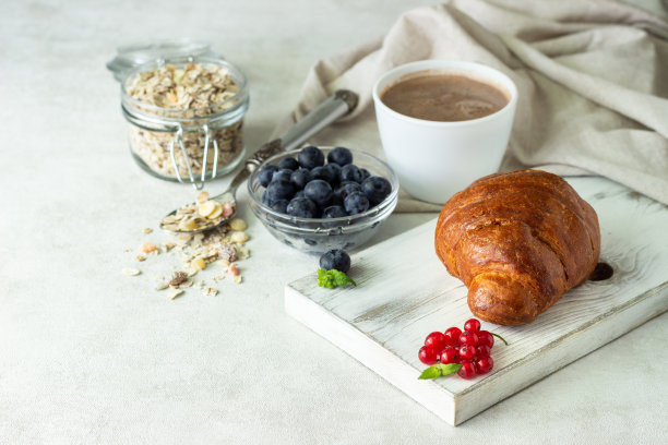 有新鲜浆果的羊角面包，什锦麦片和一杯咖啡或热巧克力在一个明亮的背景。副本的空间。图片下载
