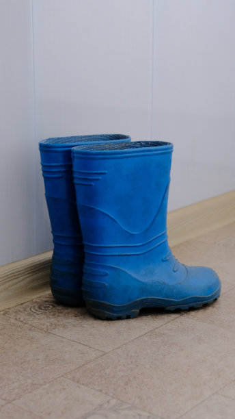 一双蓝色的儿童胶靴，沿着白色的墙，铺着油毡图片下载