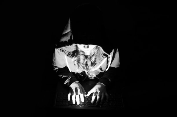 戴着兜帽的黑客女孩在黑暗中用笔记本电脑工作图片下载