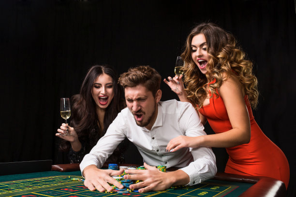 两个年轻的女人和男人在轮盘赌桌子后面黑色的背景图片下载