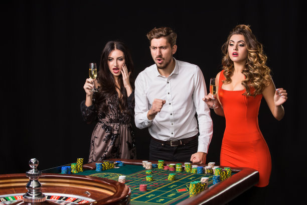 两个年轻的女人和男人在轮盘赌桌子后面黑色的背景图片下载