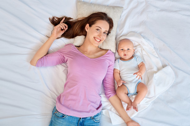 婴儿护理。年轻的母亲和小儿子一起躺在床上开心地俯视图微笑着图片下载