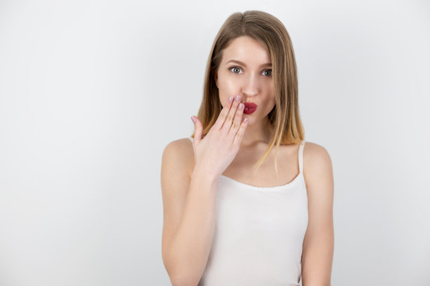 年轻漂亮的金发女人显得害羞，触摸她的脸，站在孤立的白色背景上，肢体语言图片下载