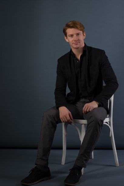 摄影棚拍摄了一个英俊的年轻人坐在椅子上看着相机图片下载