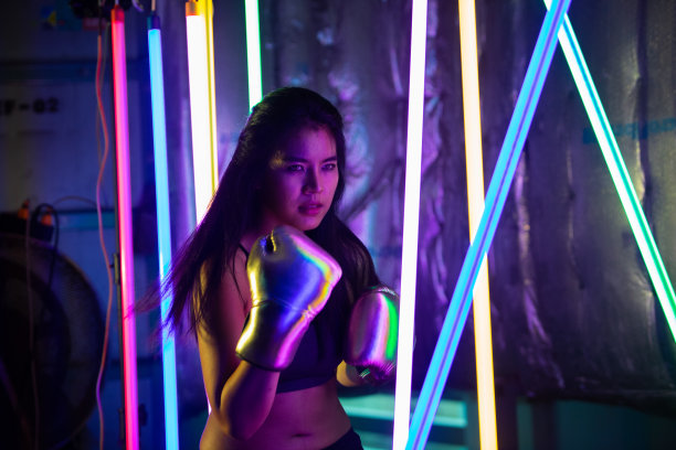 美丽的亚洲女人正在训练，戴着银色金色手套进行拳击。上班族在现代彩色霓虹泰拳拳击馆锻炼，汗水飞溅图片下载