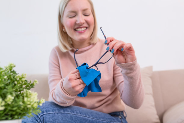 用布擦老花镜的女人。女人用蓝布手工清洁眼镜镜片。图片下载