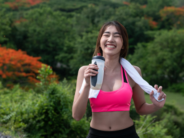 在早晨的阳光下，年轻的亚洲妇女在马路上跑步后喝水。女性慢跑锻炼。健康生活方式图片下载