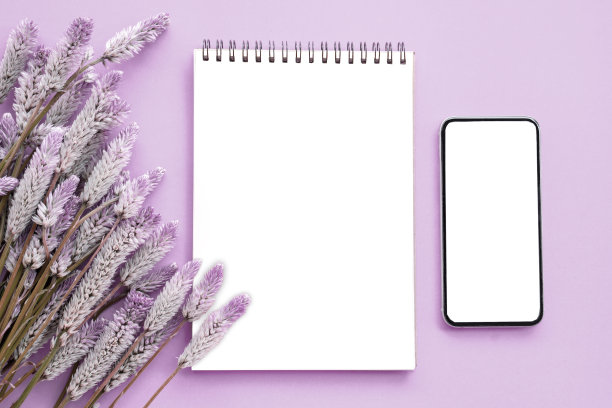 带花的记事本和智能手机平铺构图在紫色的背景上图片下载