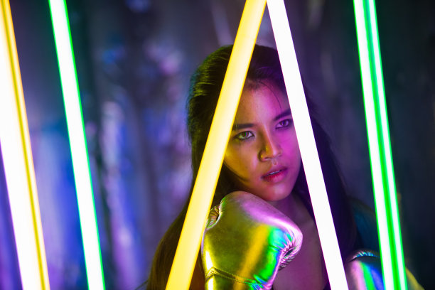 美丽的亚洲女人正在训练，戴着银色金色手套进行拳击。上班族在现代彩色霓虹泰拳拳击馆锻炼，汗水飞溅图片下载