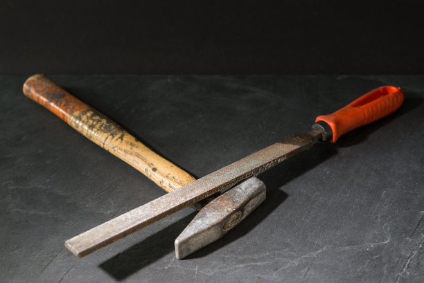 一把锤子和一把锉刀放在一块深色的石头上图片下载