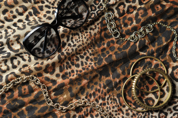 豹纹面料占据了整个框架的空间。手镯、铁链和太阳镜都摆在织物上。图片下载