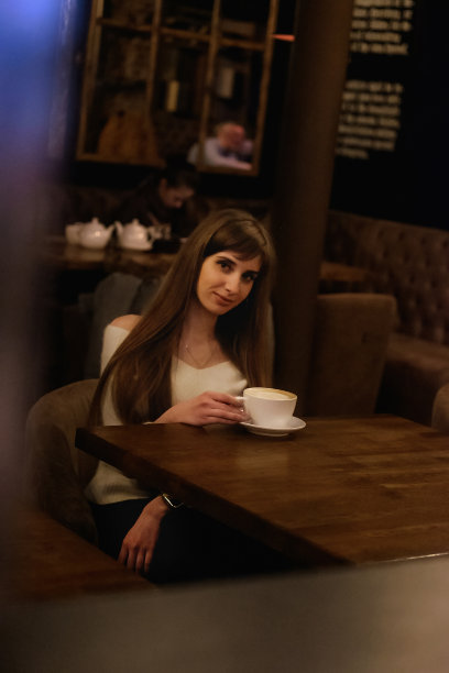 穿着白色毛衣的长发美女坐在咖啡店的一张木桌旁喝咖啡图片下载