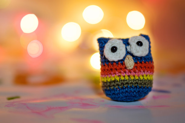 由羊毛装订猫头鹰手工制作的节日背景，以散焦灯为背景图片下载