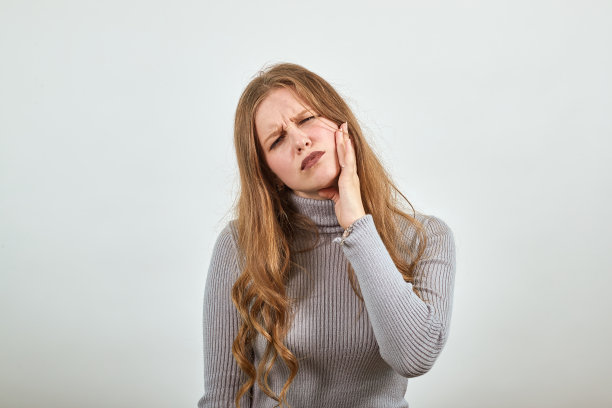 红发年轻女子穿着灰色毛衣，牙痛难忍图片下载