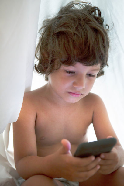 快乐的小男孩把智能手机放在羽绒被下图片下载