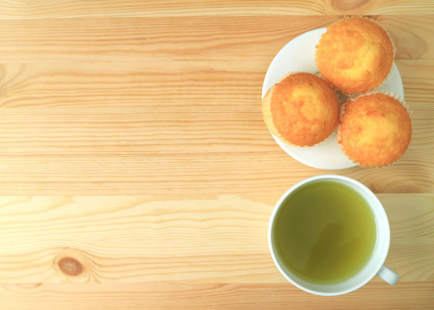 顶视图一盘马德琳纸杯蛋糕与一杯绿茶在木桌子上图片下载