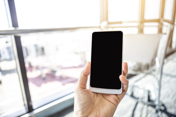 女孩手持智能手机，背景为模糊的机场图片下载