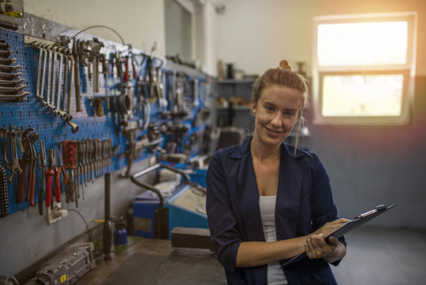 年轻的女学徒机修工拿着剪贴板，对着镜头微笑。图片下载