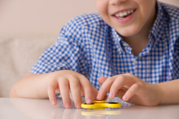 儿童的手指拨动指尖陀螺特写。微笑的男孩玩着黄色指尖陀螺玩具图片下载