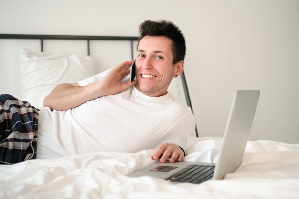 穿着白衬衫和睡衣的年轻人坐在床上看着屏幕，手里拿着银行卡图片下载